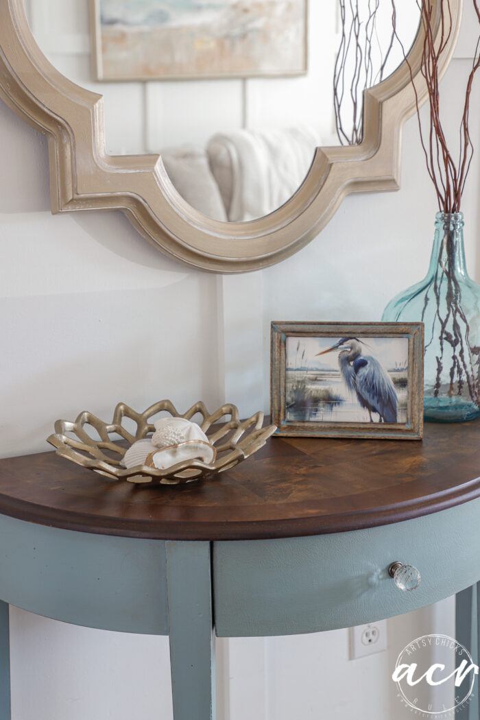 up close of coastal decor blue heron framed print, gold boat with shells and blue glass vase