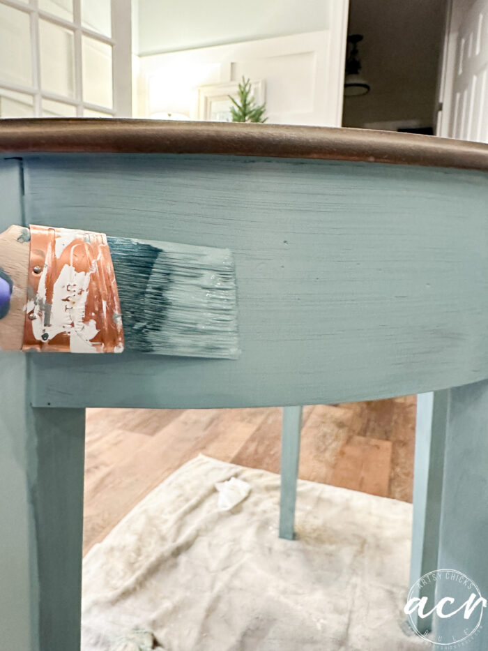 paintbrush brushing blue paint on side of table