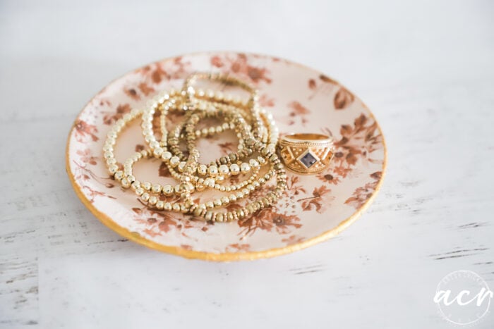 small decoupaged saucer with gold bracelets and gold ring