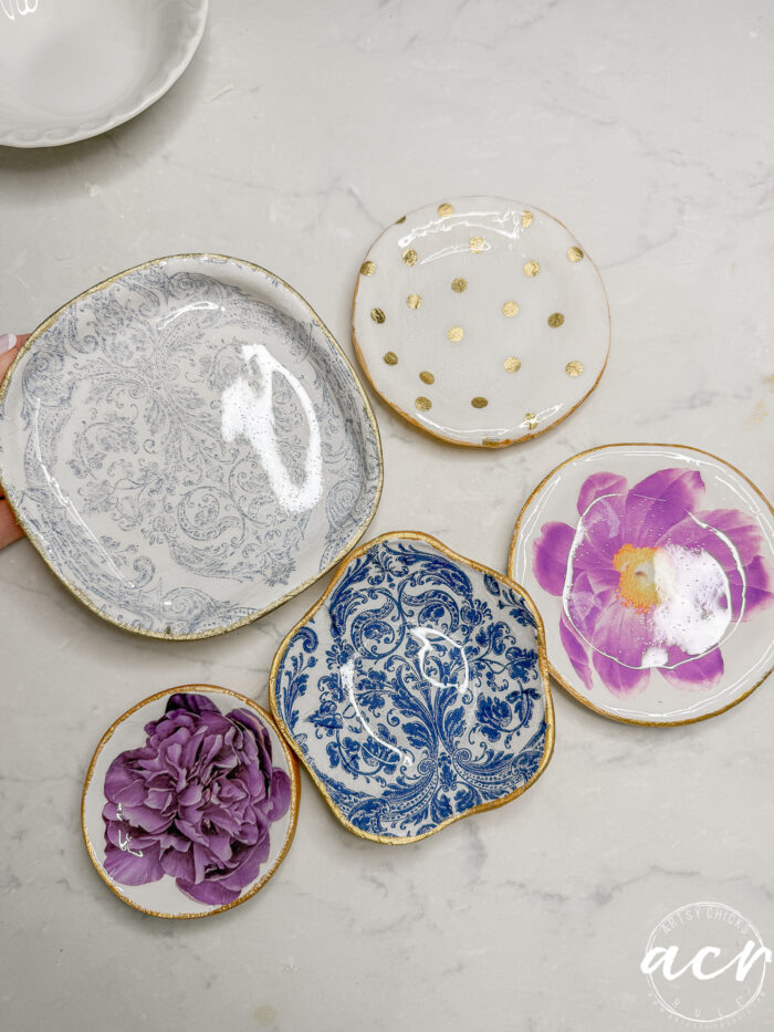Five decorative ceramic plates are arranged on a light surface. Alongside their blue floral and gold polka dot designs, they inspire ideas for handmade crafts like decoupage earrings or learning how to use UV resin for unique creations.