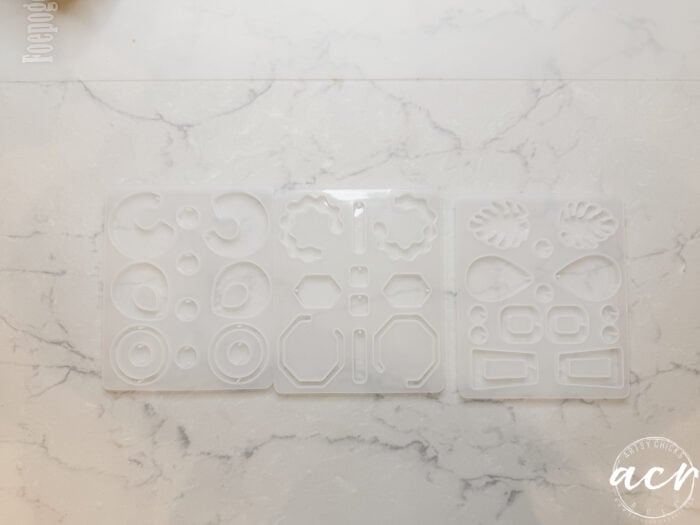 Three clear silicone molds for jewelry making are arranged on a light marble surface. Each mold features geometric and abstract shapes, perfect for crafting UV resin or decoupage earrings. Ideal for anyone learning how to use silicone molds creatively.