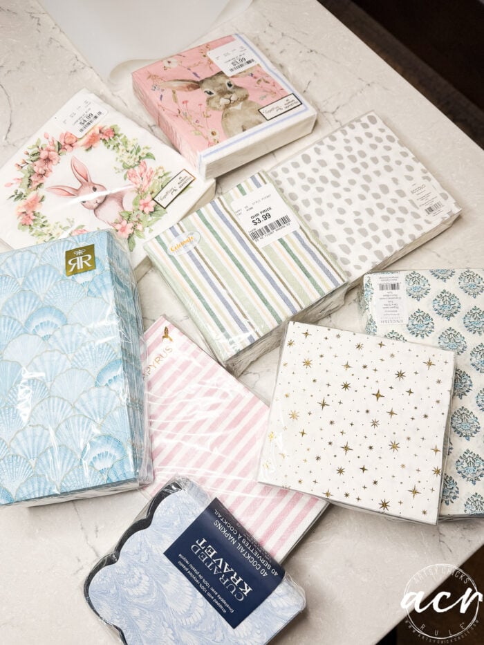Various decorative napkin packs arranged on a marble surface, featuring patterns like bunnies, pink stripes, stars, and seashells—perfect for decoupage earrings or learning how to use UV resin in creative crafts.