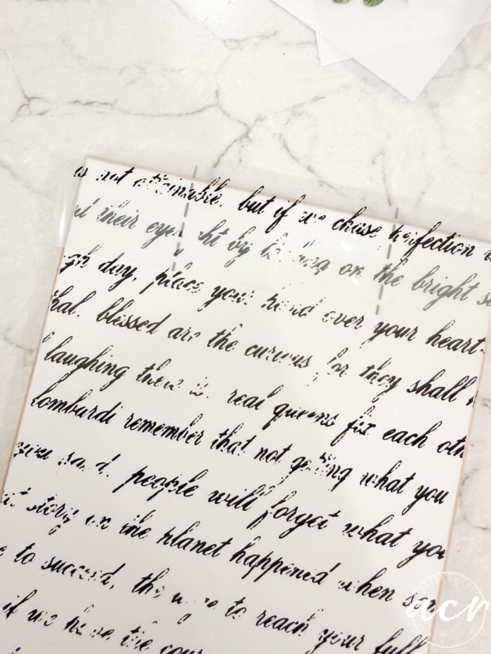 A sheet of white paper with cursive black script, partially faded and distressed, lies on a white marble surface&mdash;an Easter Edition by Flipping Smalls. Some words are missing or hard to read, giving it a vintage, worn effect.