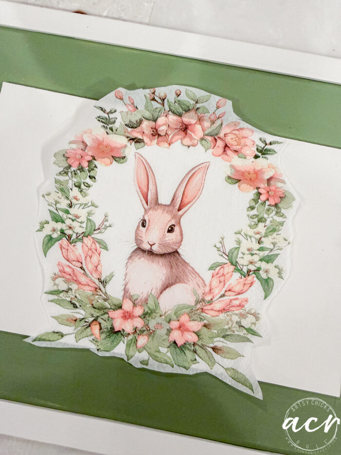 A watercolor illustration of a brown rabbit sits in the center of a floral wreath made of pink flowers and green leaves, displayed on a white and green background&mdash;perfect for the Flipping Smalls Easter Edition.
