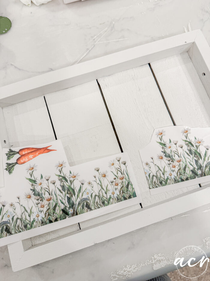 A white wooden tray being decorated with floral and carrot-themed paper cutouts, featuring daisies and carrots on a marble surface&mdash;perfect for your Easter Edition of Flipping Smalls.