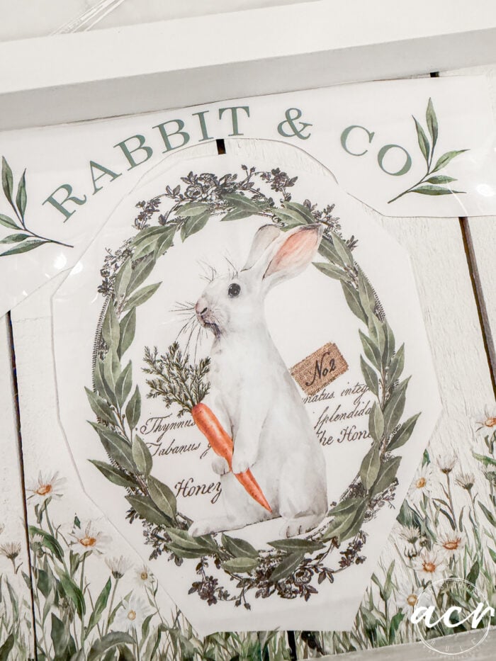 A vintage-style illustration of a white rabbit holding a carrot, framed by a green leafy wreath, with "RABBIT & CO" above and botanical accents&mdash;part of the Flipping Smalls Easter Edition collection.