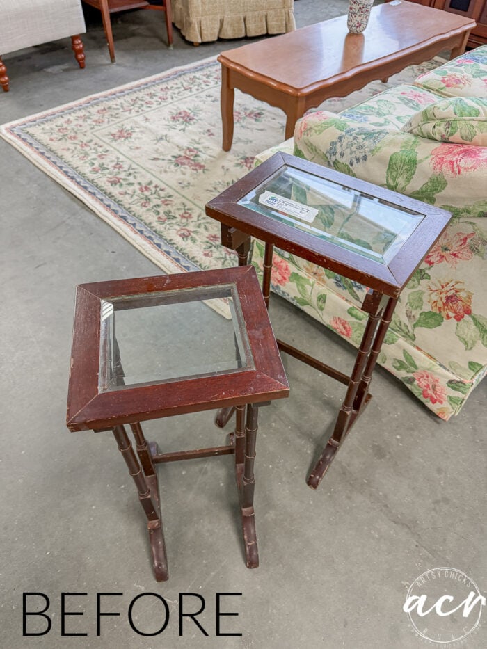 Two small glass topped nesting tables sit on a concrete floor. In the background, a floral sofa, coffee table, and patterned rug add charm. The word BEFORE appears in the bottom left corner.