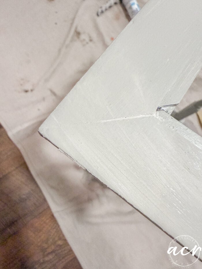 A close-up of a light-colored wooden table corner with a visible crack running through it, resting on a cloth drop sheet over a wooden floor&mdash;perfect for pairing with Glass Topped Nesting Tables in any stylish space.