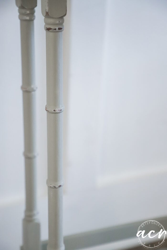 Close-up of two light-colored, painted wooden table legs with a bamboo-like design from stylish glass topped nesting tables, set against a plain white background. The bottom right corner features a circular watermark with the letters acv.
