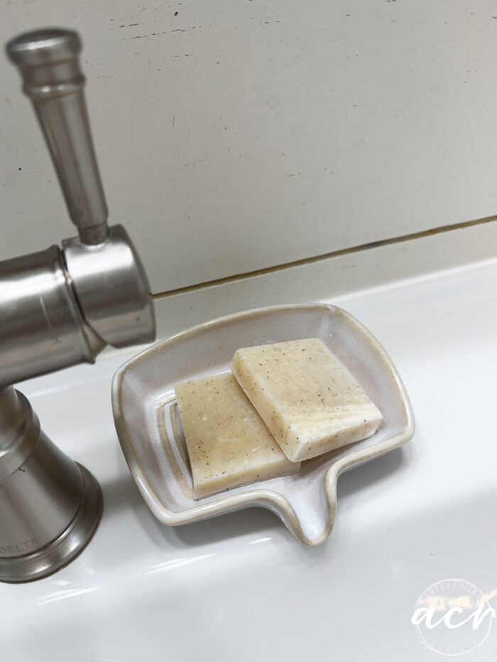 A beige soap dish holding two bars of speckled soap sits on a white sink next to a silver faucet&mdash;just one of the things I'm loving right now.