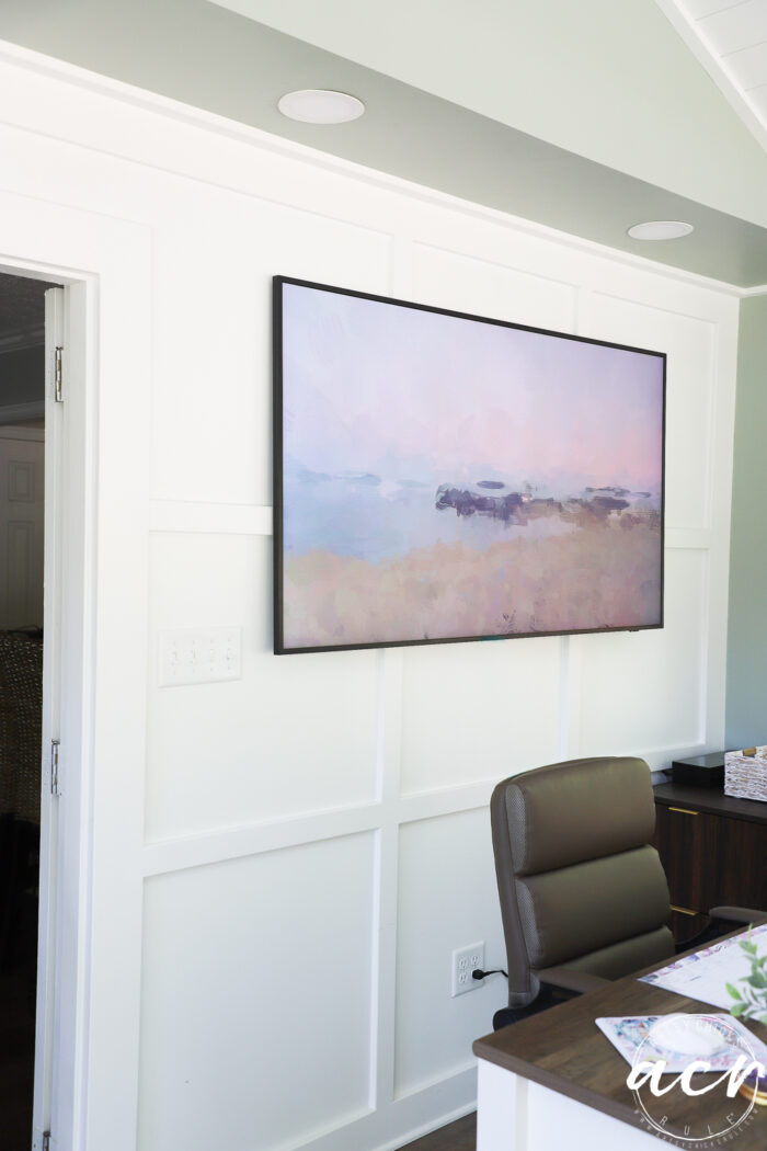 A modern office area with a brown chair, wooden desk, and a large abstract landscape painting in soft pastel colors hanging on a white paneled wall&mdash;perfect for an inspiring Office Reveal.