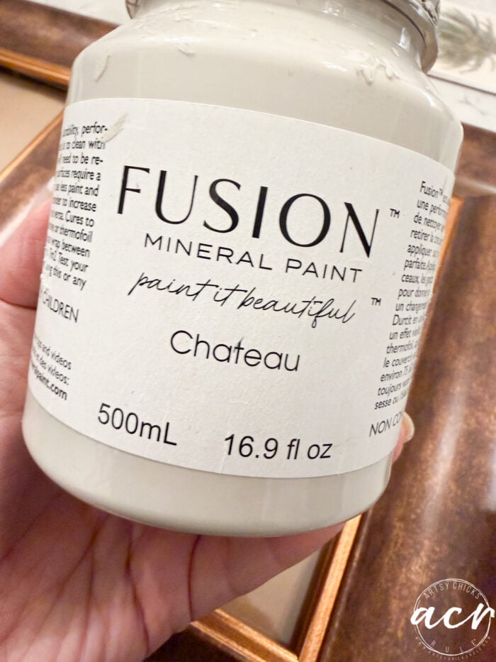 A hand holds a jar of Fusion Mineral Paint in the color Chateau, labeled 500 mL (16.9 fl oz), ideal for upcycled projects, with “paint it beautiful” written on the label.
