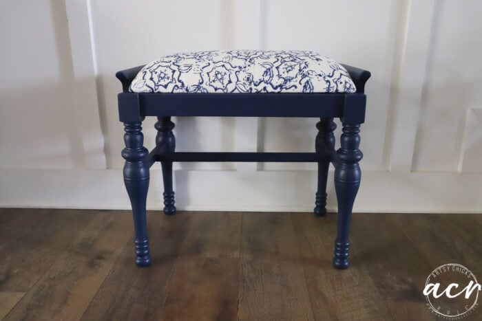 A charming vintage bench with turned legs, a white cushioned seat featuring a blue floral pattern, and a navy blue finish&mdash;this piece brings timeless vintage furniture style to any space.