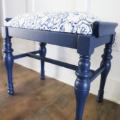 Vintage Bench Update A vintage bench with turned legs, featuring a navy blue finish and a cushioned seat upholstered in white fabric with a blue abstract pattern, sits on a wooden floor near a white paneled wall.