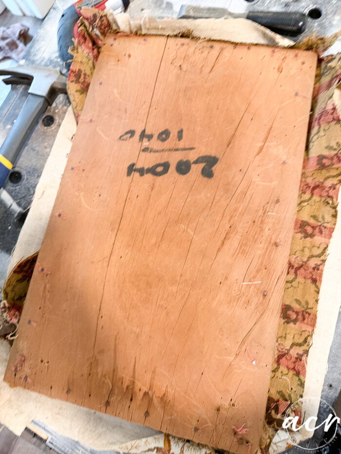 A vintage bench shows its age&mdash;a piece of worn wood with faded writing and numbers sits on old, patterned fabric, surrounded by tools and workshop materials, awaiting a thoughtful bench update.