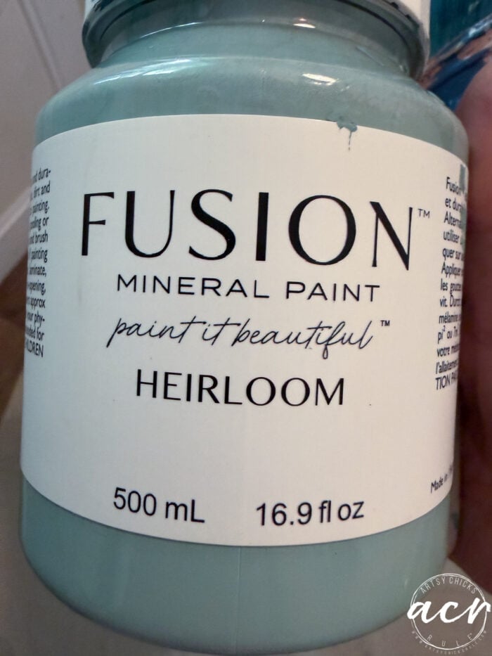 A close-up of a jar of Fusion Mineral Paint in Heirloom, perfect for refreshing your end table. The 500 ml (16.9 fl oz) jar features the soft blue-green shade with the label “paint it beautiful.”.