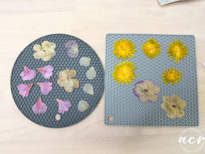 Two silicone mats with pressed flowers&mdash;purple and light yellow petals on the left, yellow and pale purple on the right&mdash;are arranged neatly on a wooden surface, perfect for crafting unique flower petal resin earrings.