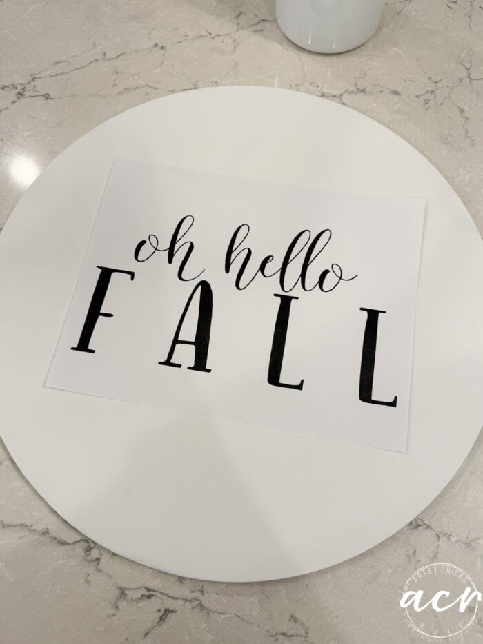 A white card on a round white tray reads “oh hello FALL” in cursive and bold letters, reminiscent of a charming Fall Door Hanger, placed elegantly on a marble surface.