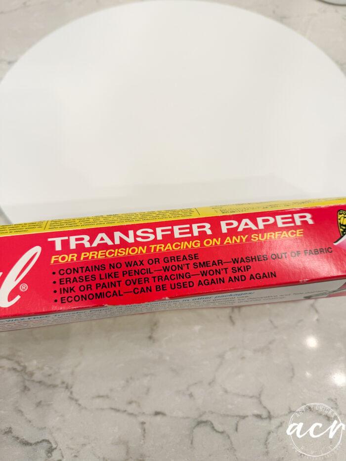 A yellow and red box labeled TRANSFER PAPER for precision tracing on any surface sits on a marble countertop with product features listed in white and black text—perfect for designing your own Fall Door Hanger or adding custom lettering to an “Oh Hello Fall” sign. A white round plate is visible in the background.