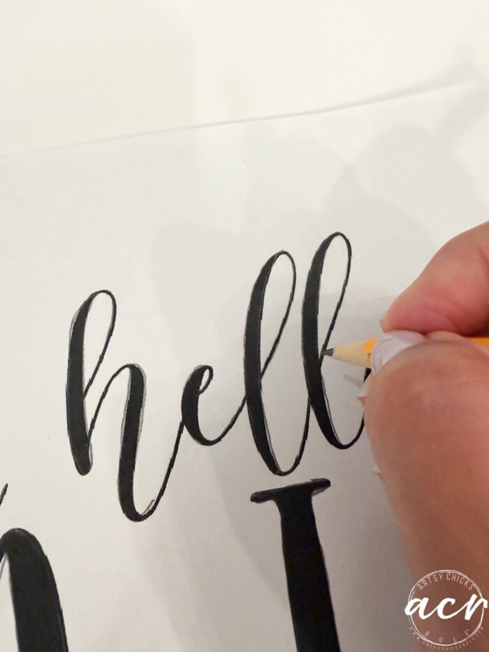 A hand traces the word hello in black cursive on white paper with a pencil, evoking the welcoming charm of a Fall Door Hanger. An acn watermark is visible in the bottom right corner.
