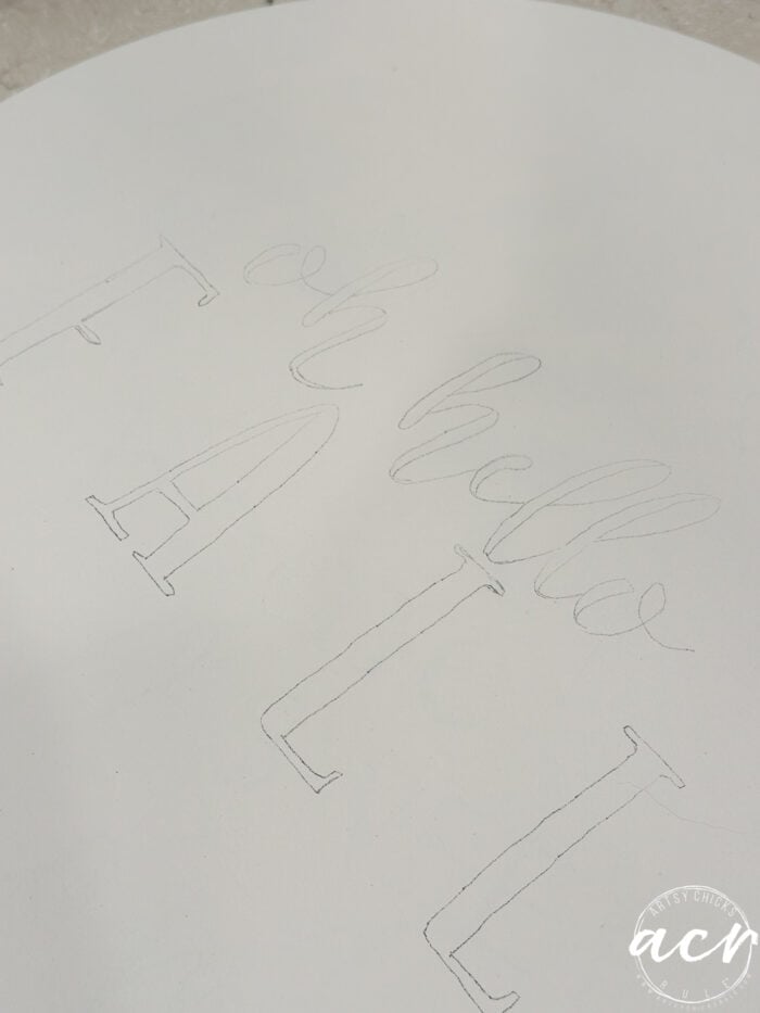 A white surface with lightly penciled, hand-drawn letters spelling oh hello FALL in a mix of cursive and block fonts creates the perfect design for an inviting Fall Door Hanger.