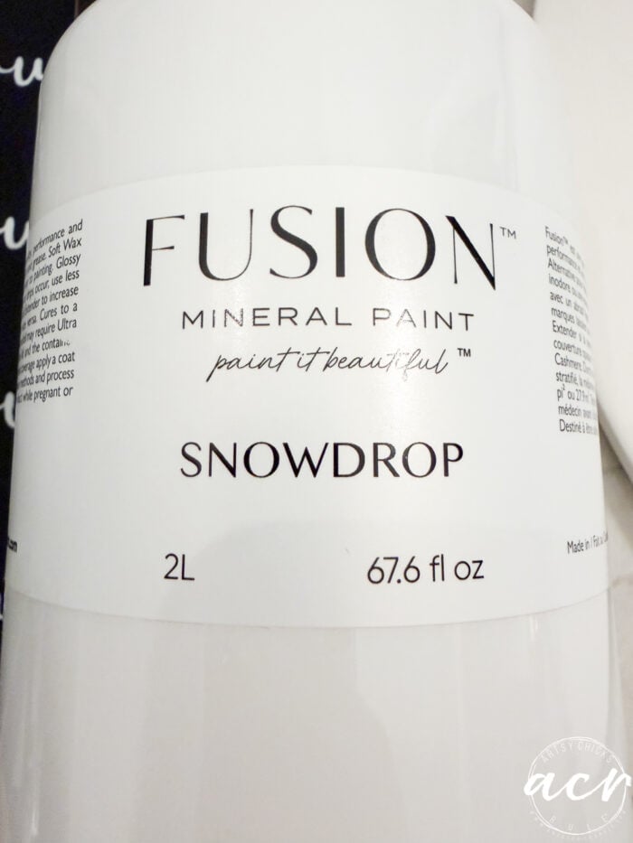 A close-up of a white container labeled FUSION MINERAL PAINT in the color Snowdrop, with 2L and 67.6 fl oz printed below. The label also says paint it beautiful—perfect for creating a charming fall door hanger or adding a fresh touch to your autumn door decor.