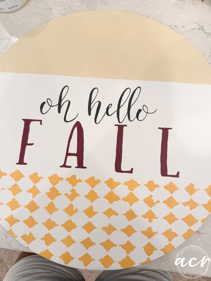 A round Hello Fall sign with “oh hello FALL” written on it, featuring a beige top, white middle, and yellow patterned bottom section. The word FALL is in large, bold letters—perfect as a cheerful Fall Door Hanger to welcome the new season.