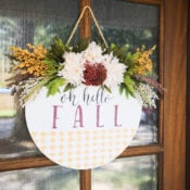 Oh Hello Fall Door Hanger A round wooden sign, perfect as a Fall Door Hanger, features elegant flowers and leaves surrounding the words “oh hello FALL” in flowing script. Hanging on a door, this charming piece is accented by a gold diamond pattern along the bottom, creating a warm and inviting seasonal welcome.