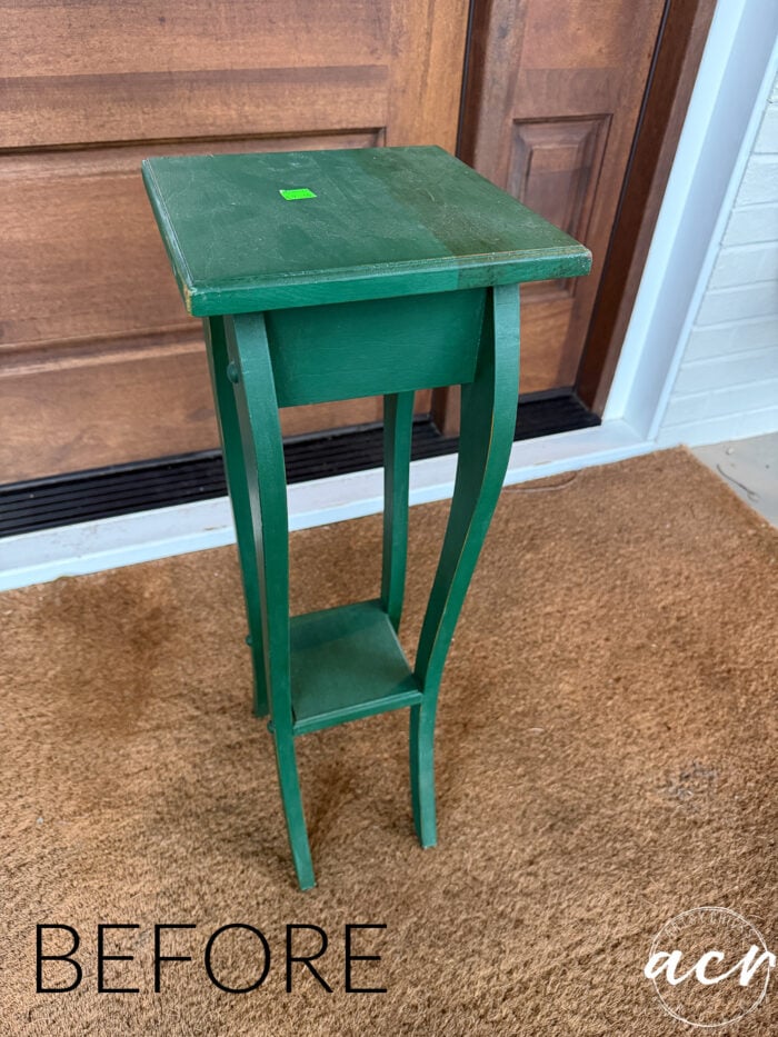 A petite table makeover is on display as a small green wooden plant stand with curved legs sits on a brown doormat in front of a wooden door. The word BEFORE is written in the lower left corner.