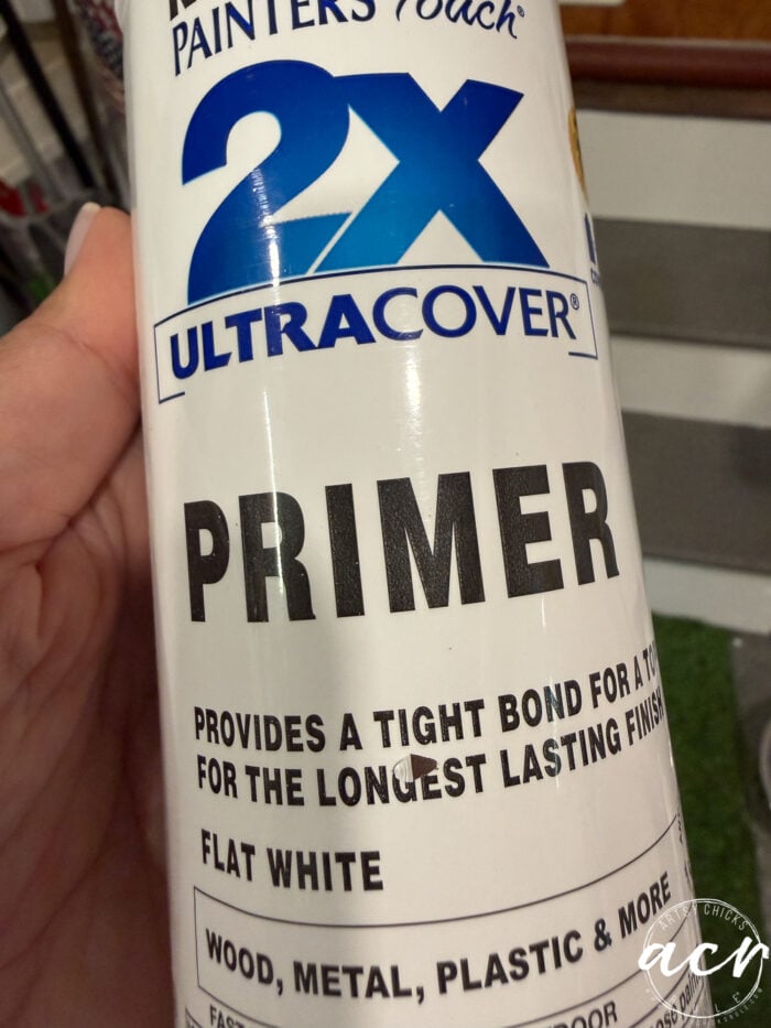 Hand holding a can of 2X Ultra Cover Primer spray in Flat White, labeled for use on wood, metal, plastic, and more—perfect for your next Petite Table Makeover. Text highlights strong bonding and long-lasting finish.