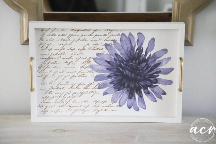 A white tray with gold handles, featuring a large purple flower and cursive script in brown ink as the background—a charming accent piece perfect for your next petite table makeover or furniture restoration project.