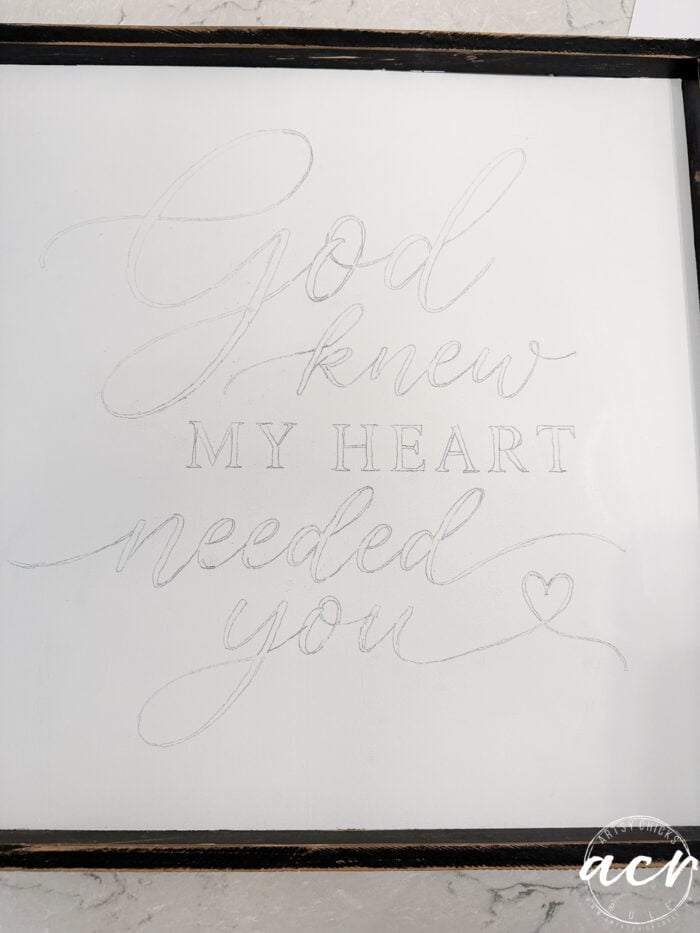 A thrifted redo features a white sign with cursive pencil writing that reads, God knew my heart needed you, ending with a small heart. The letters appear faint and unfinished, giving the God Knew My Heart Needed You sign a delicate, handmade charm.