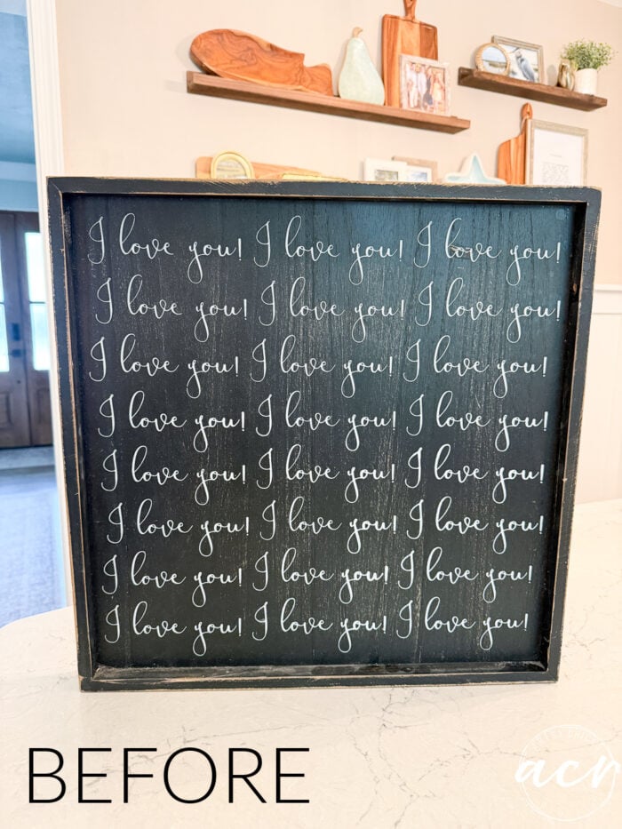 A black framed sign with I love you! written repeatedly in white cursive. The word BEFORE appears in black text at the bottom left corner of the image, hinting at a possible thrifted redo transformation. Decor items are visible in the background, setting the stage for a charming update—perhaps even into a sentimental God Knew My Heart Needed You Sign.