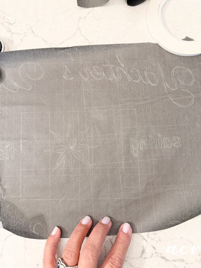 A hand holds a piece of transfer tape with faint outlines for lettering and a star design, placed on a white surface—perfect for creating your own God Knew My Heart Needed You Sign or an inspired thrifted redo. Some rolls of tape are visible at the top.