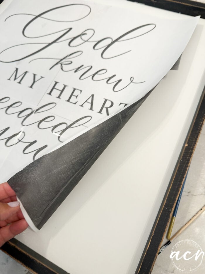 A hand lifts a printed sheet that reads, God knew my heart needed you, partially revealing a blank canvas underneath with a pencil lying beside the canvas—a charming scene perfect for home decor or as inspiration for your next thrifted redo.