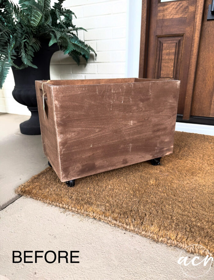 A brown, worn wooden box on wheels sits on a doormat in front of a door, styled as a charming Harvest Crate with a green plant nearby. The word BEFORE appears in the bottom left corner, evoking cozy Fall Decor.