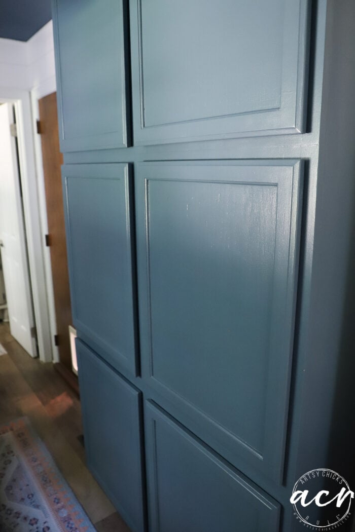 A close-up of a blue paneled wall with a smooth, glossy finish, located in a hallway with a wooden floor and partially visible doors in the background—an ideal setting for a laundry room or as inspiration for your next wood countertop update.