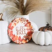Three pumpkins, two white and one brown, crafted from Air Dry Clay, sit beside a small decorative plate with hello FALL text and autumn leaves. A white vase with dried grasses is in the background on a light wooden surface, illustrating a creative comparison of clay brands in stylish autumn decor.