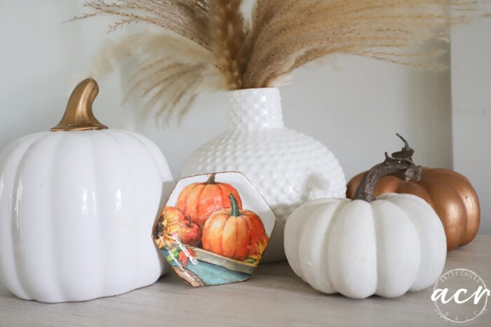 White and bronze pumpkins, a small decorative plate with painted pumpkins crafted using Air Dry Clay, and a white vase with pampas grass create a cozy autumn display on a white surface.