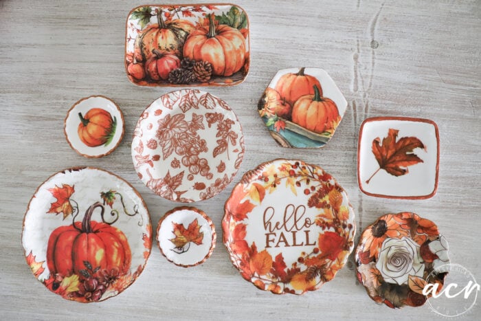 A set of autumn-themed plates crafted from the best air dry clay, featuring pumpkins, leaves, and hello FALL designs arranged on a light wooden surface.