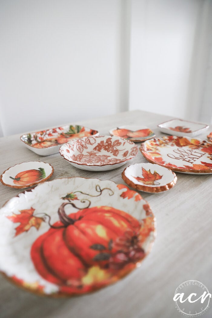 A set of decorative plates with autumn and pumpkin designs in orange and brown tones, crafted using air dry clay, are arranged on a light-colored table.