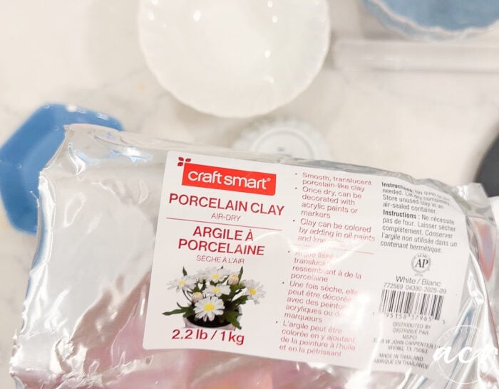 A 2.2 lb (1 kg) package of Craft Smart air-dry porcelain clay sits on a surface with the label visible, showing white daisies and product information in English and French—an ideal choice for anyone exploring top Clay Brands in an Air Dry Clay comparison.