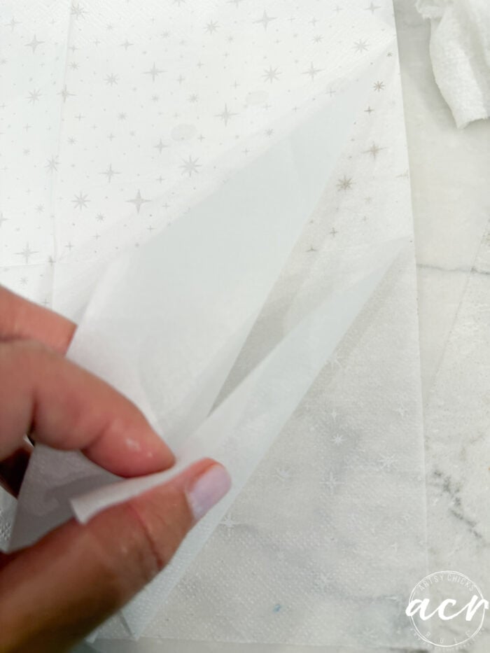 A hand peels apart two layers of a white paper napkin with a small star pattern, on a marble surface—capturing the delicate attention to detail that makes Flipping Smalls #4 truly unique among flipping collectibles.
