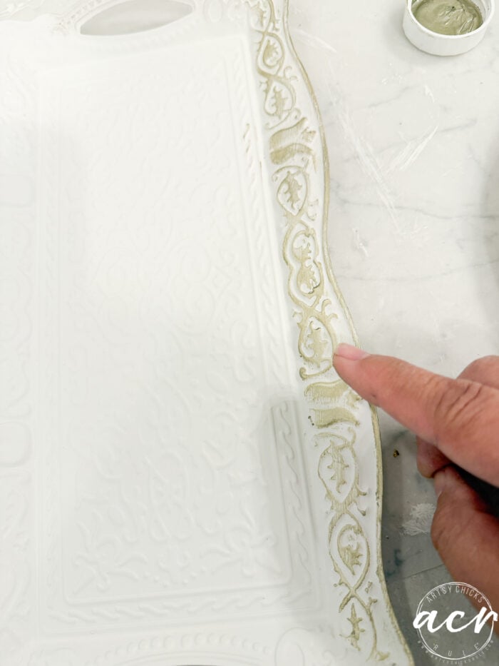A hand uses a small brush to paint gold accents on the ornate edge of a white decorative tray, which is resting on a white surface—a delicate detail captured as part of the Flipping Smalls #4 collection.