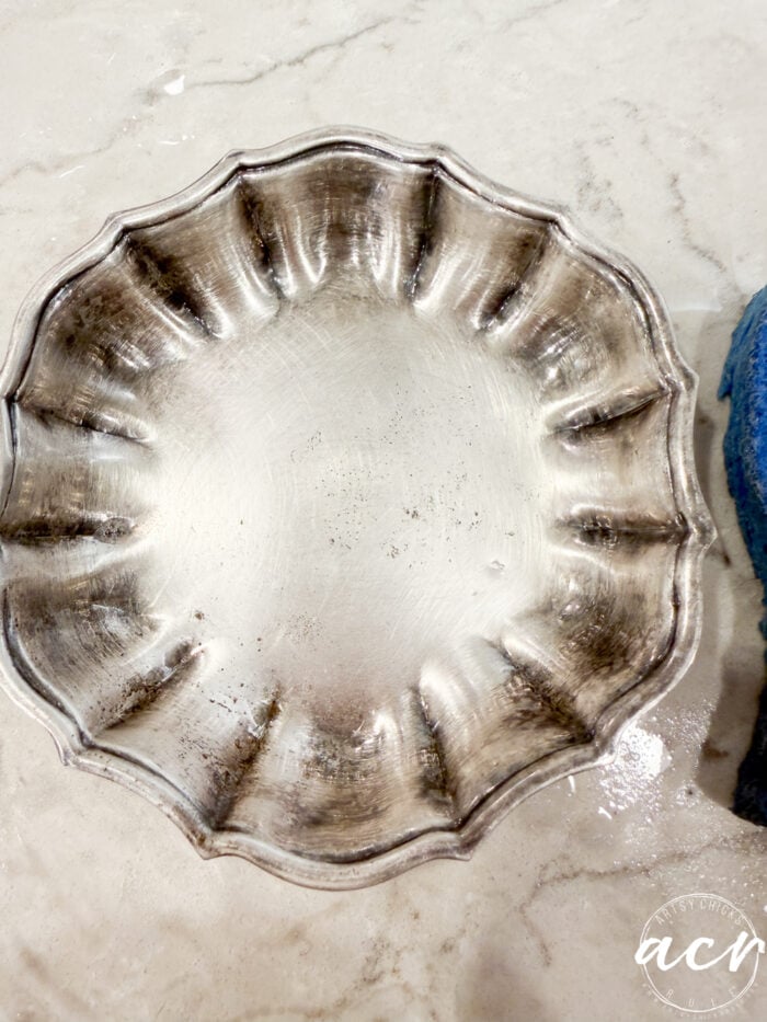 A tarnished silver scalloped dish sits on a marble surface. The edges are darkened, showing signs of oxidation, and a blue cleaning cloth is partially visible on the right side of the image—a perfect scene for Flipping Smalls enthusiasts searching for their next restoration project.