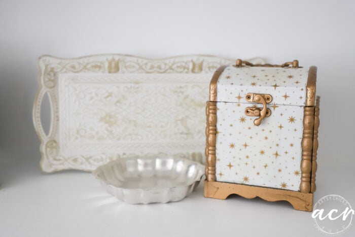 A white and gold decorative chest, a scalloped silver dish, and an ornate rectangular tray from Flipping Smalls are displayed on a white surface.
