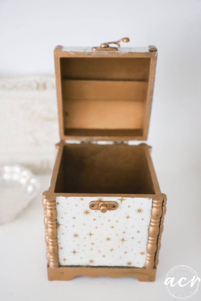 A small, open wooden box painted gold with white panels decorated with gold stars, sitting on a white surface—an eye-catching addition to any collectibles display and part of the charming Flipping Smalls #4 series.