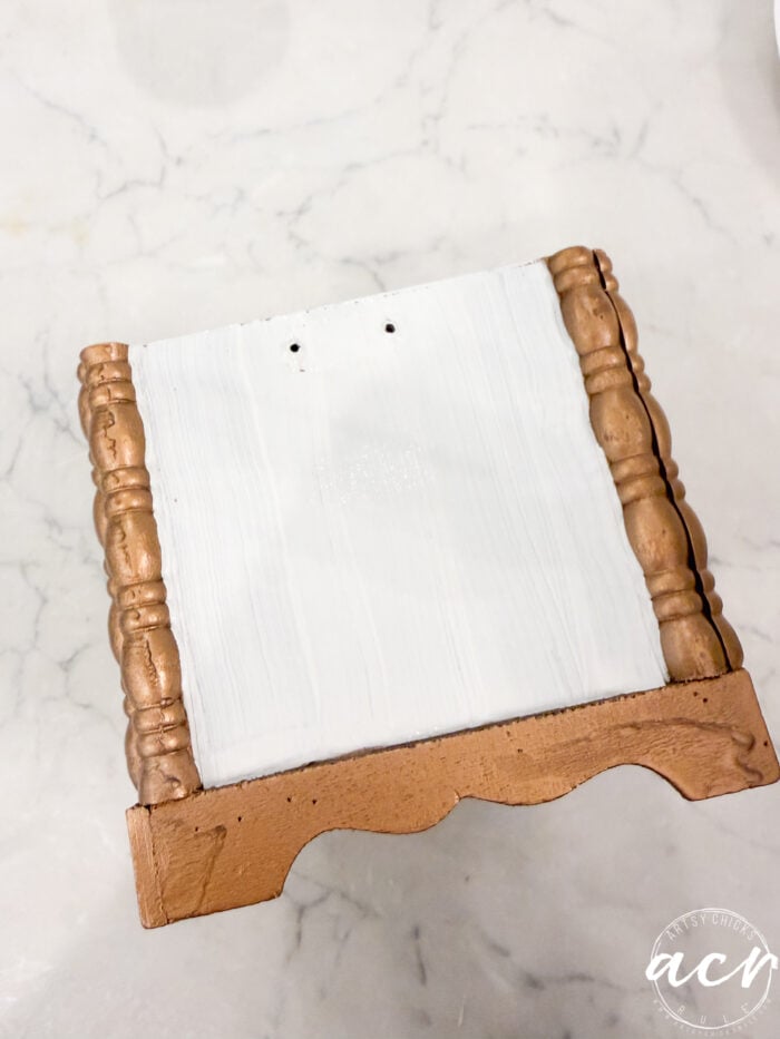A small wooden item from Flipping Smalls, with gold-painted edges and legs and a white top surface, sits on a white marble background. The ACM watermark is visible in the corner.