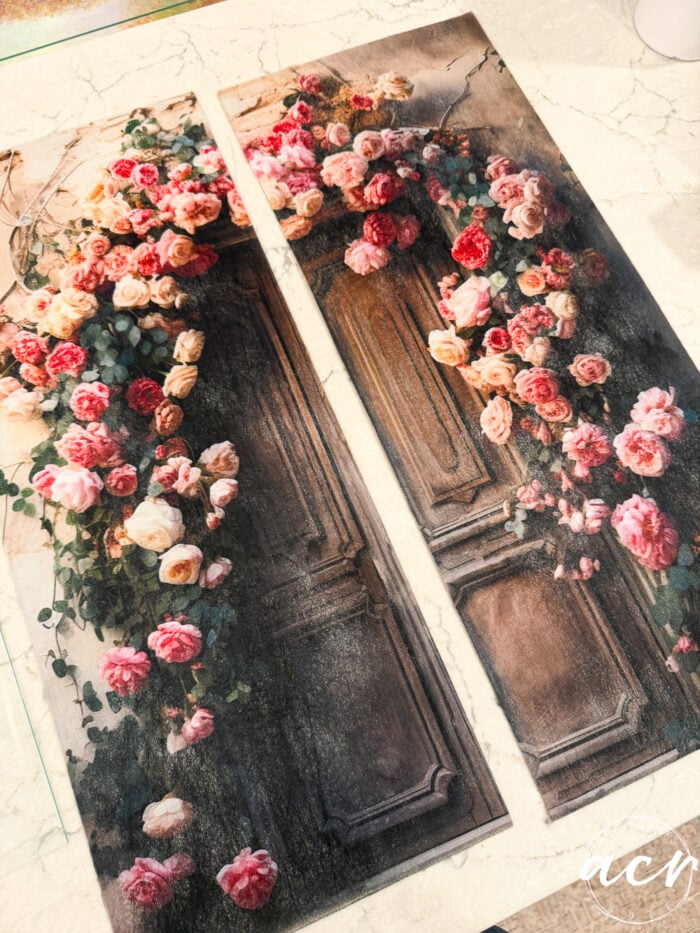 Two panels with a vintage door design, covered in pink, red, and peach roses and green foliage, are placed side by side on a light marble surface. These framed prints appear to be printed or painted artwork, bringing an updated touch of classic elegance to any space.