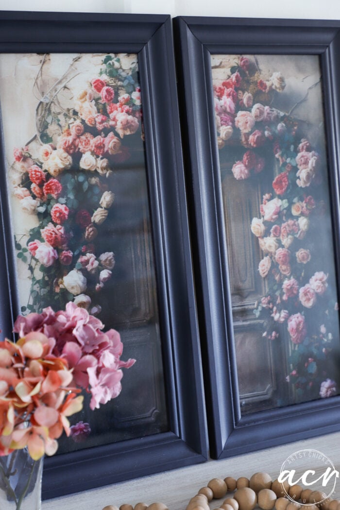 Two updated framed prints of pink and red roses cascade over a rustic door, displayed side by side. In front, a cluster of light pink hydrangeas rests beside a string of wooden beads on a light-colored surface, reminiscent of delicate tissue paper textures.